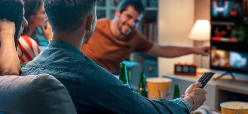 Four friends sitting on a living room couch watching TV